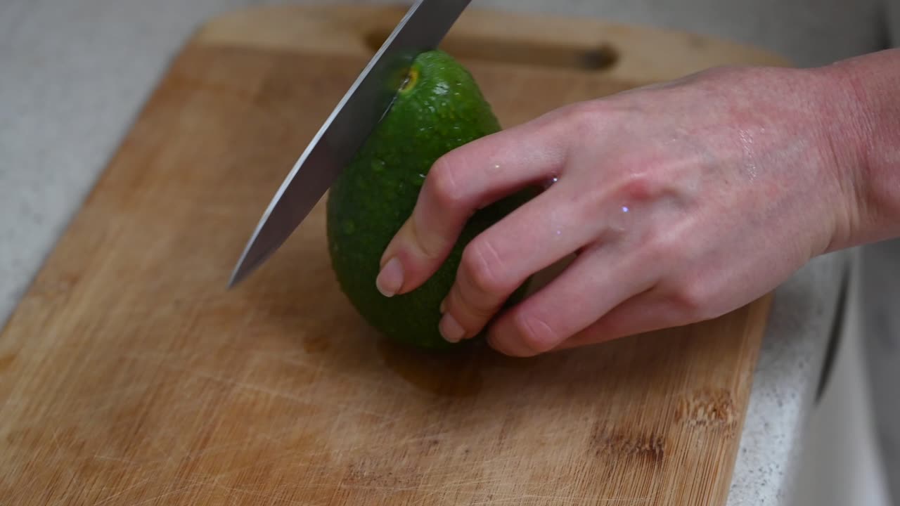 Close up of a woman cutting up an avocado on a wooden cutting board