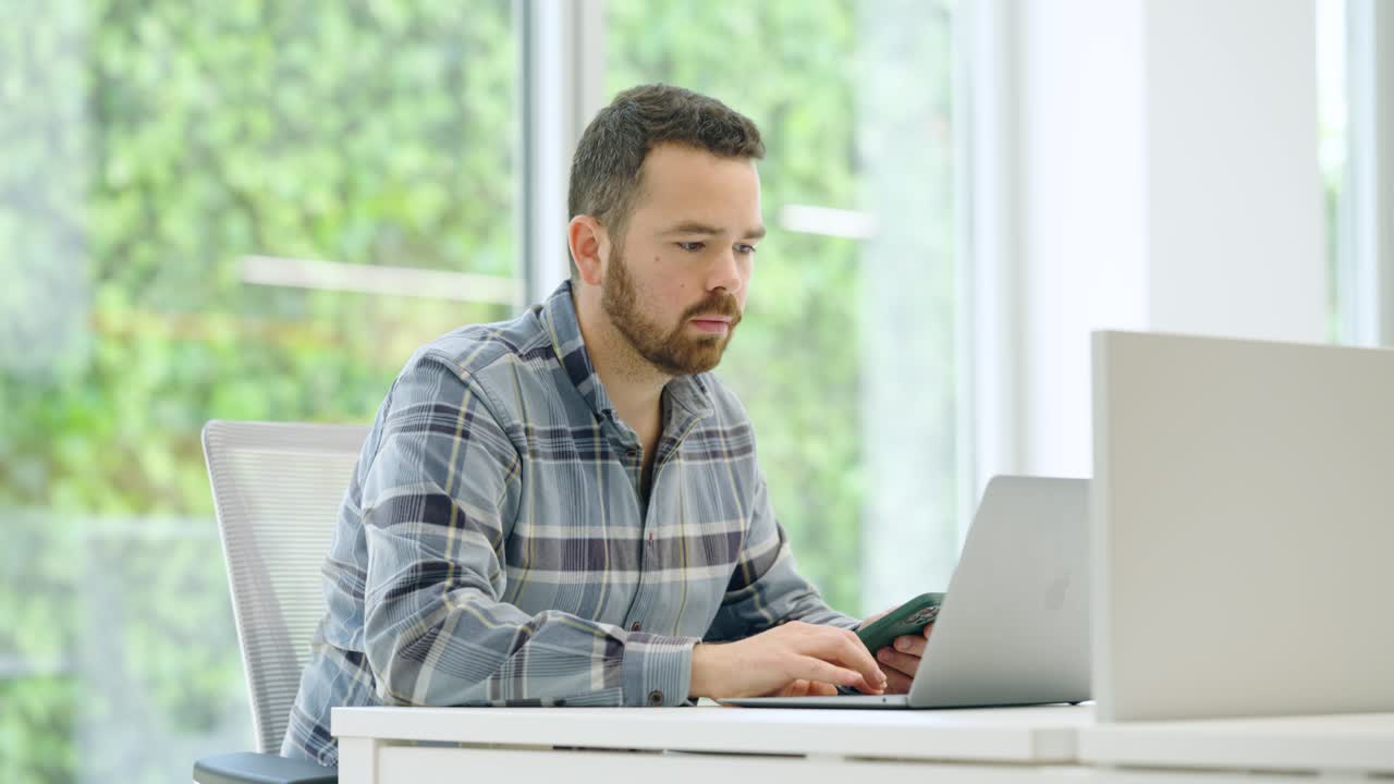 Office worker using laptop and smartphone at desk