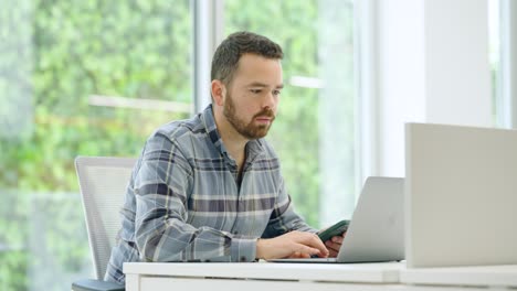 office worker using laptop and smartphone at desk