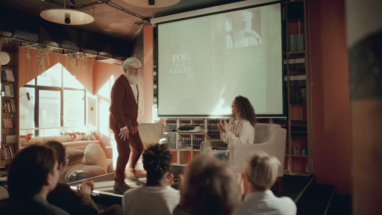 autor anciano entrando en la biblioteca, saludando a la audiencia y respondiendo preguntas