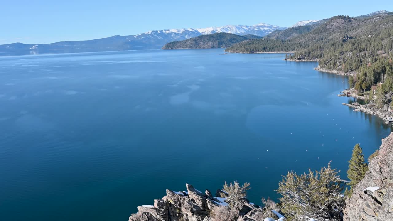 Aerial drone view of a deep blue mountain lake bordered by rocky cliffs and evergreen forest