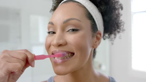 Happy-biracial-woman-brushing-teeth-in-bathroom,-slow-motion