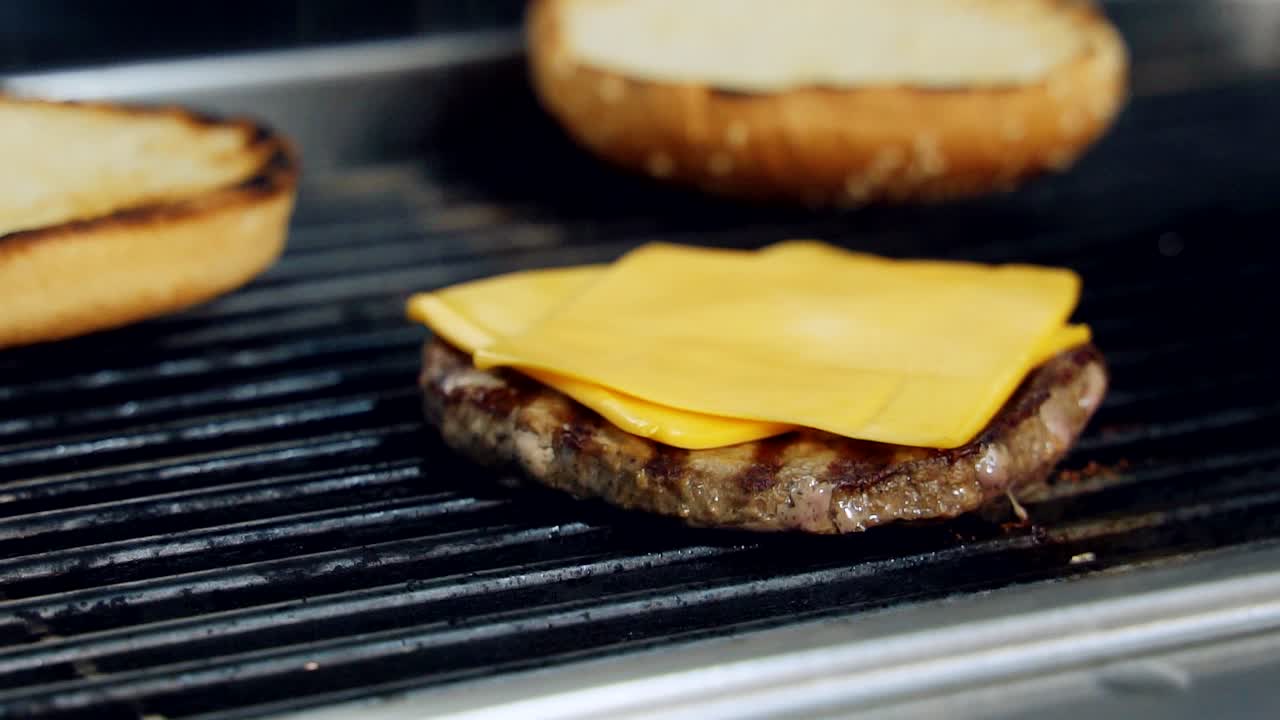 Meat cutlet with cheese is roasting on hot grill. Preparation of cheeseburger ingredients on frying grill. Making delicious fast food. Close-up