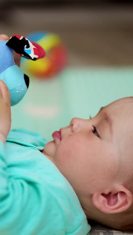 little baby boy looking earnestly on the toy in his hands. cute child waves the toy, looks into camera and shows his tongue. vertical video