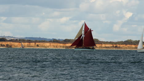 Toma-De-Un-Ferry-Catamarán-Propulsado-Por-Un-Jet-Rojo-Entrando-En-El-Marco-Frente-A-Un-Cortador-De-Garfio-Llamado-Golden-Vanity-Y-Un-Velero-En-El-Calshot-Spit-Junto-Al-Solent,-Southampton