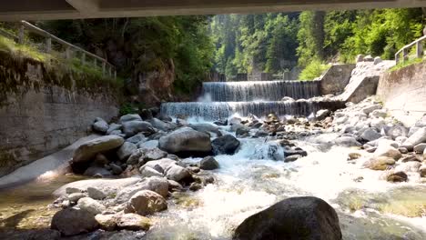 aerial dolly flying upstream a flowing creek under a wooden bridge in the forest