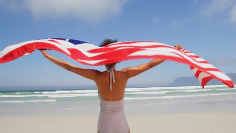 Mujer-Parada-Junto-Al-Mar-Con-Una-Bandera-Americana-Ondeando.-En-La-Playa-4k