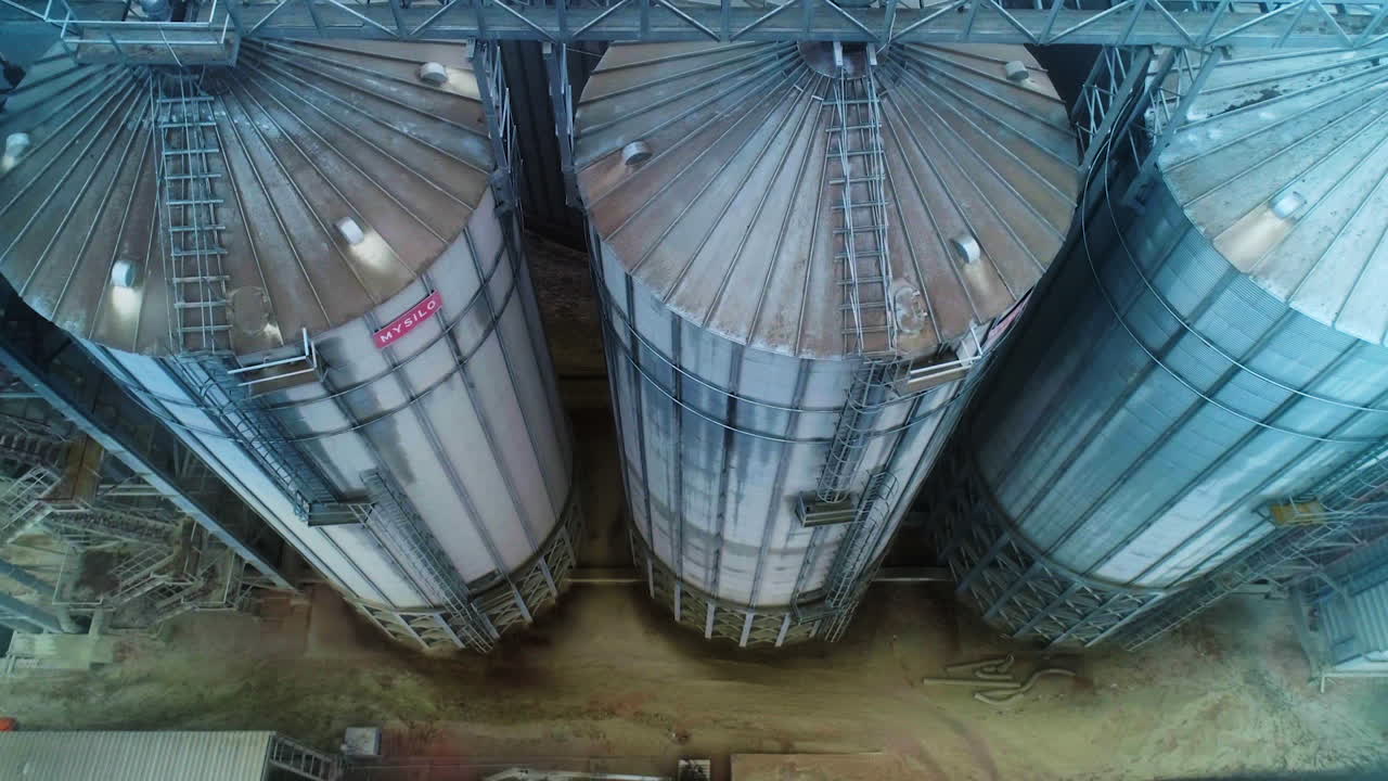 Huge mighty cisterns for grain storage at elevator plant. View on the metal tanks connected with each other by a support. Aerial perspective.