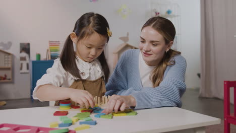 little girl in a montessori school playing with shapes stacking while teacher helping her 1