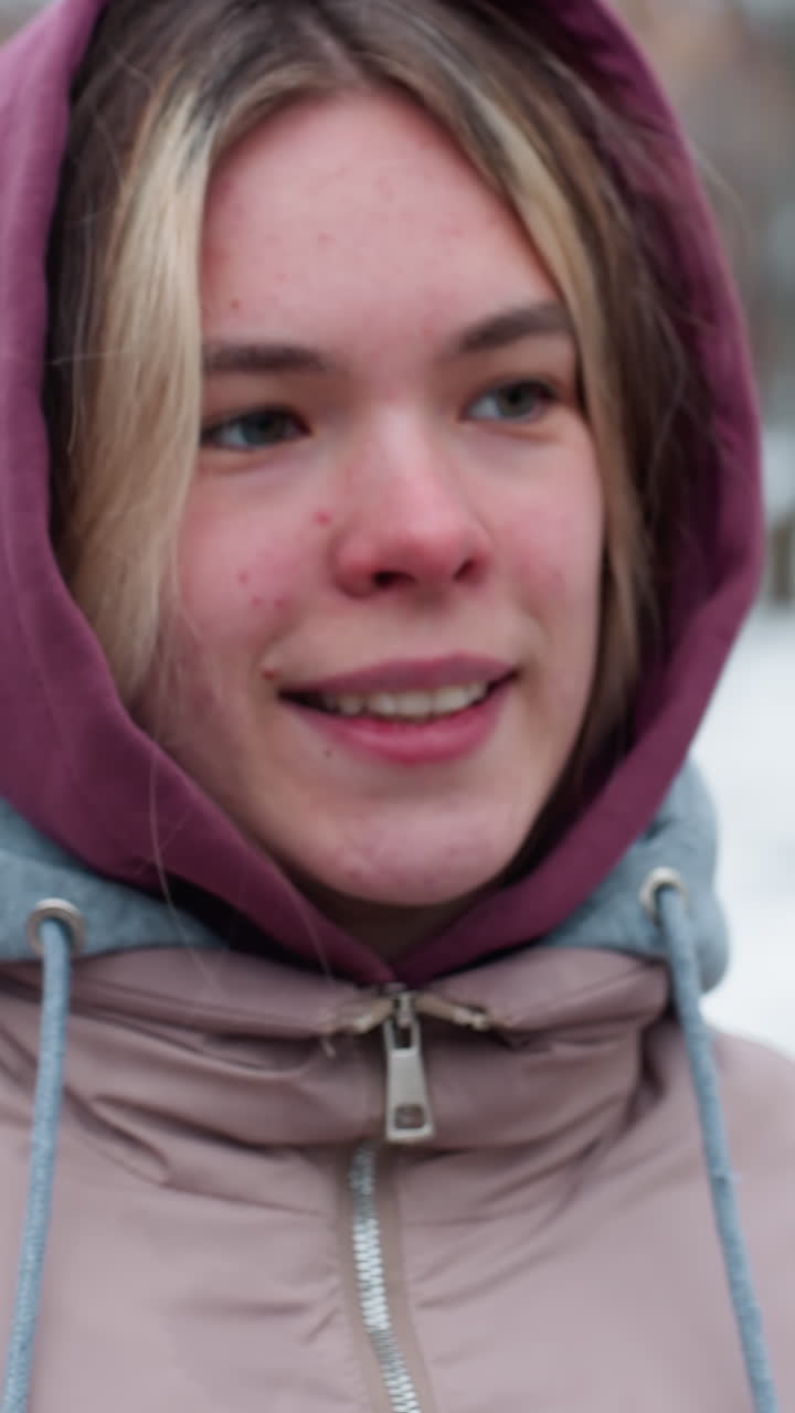 Primo piano di un giovane adulto che afferra la catena dell'altalena mentre si arrampica per mantenere l'equilibrio, indossando una calda giacca invernale con cappuccio, terreno coperto di neve e figure sfocate sullo sfondo.