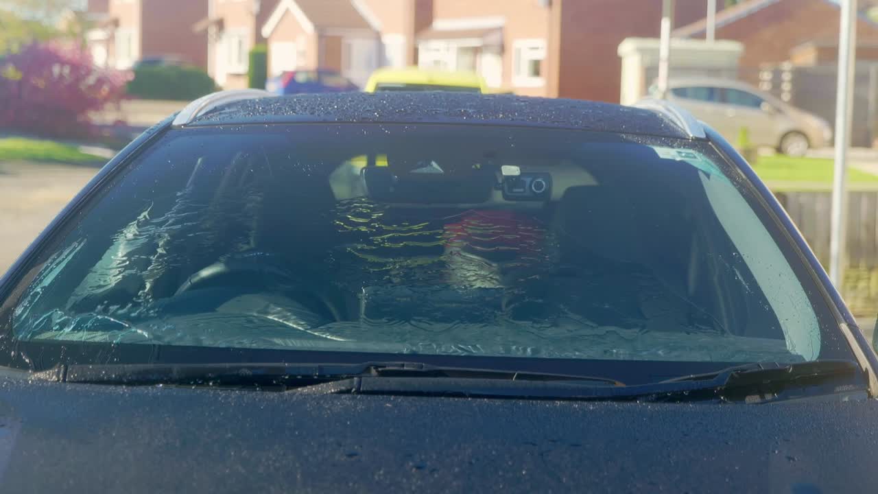 Rinsing windscreen on a black car with protection and instant water sheeting and beading