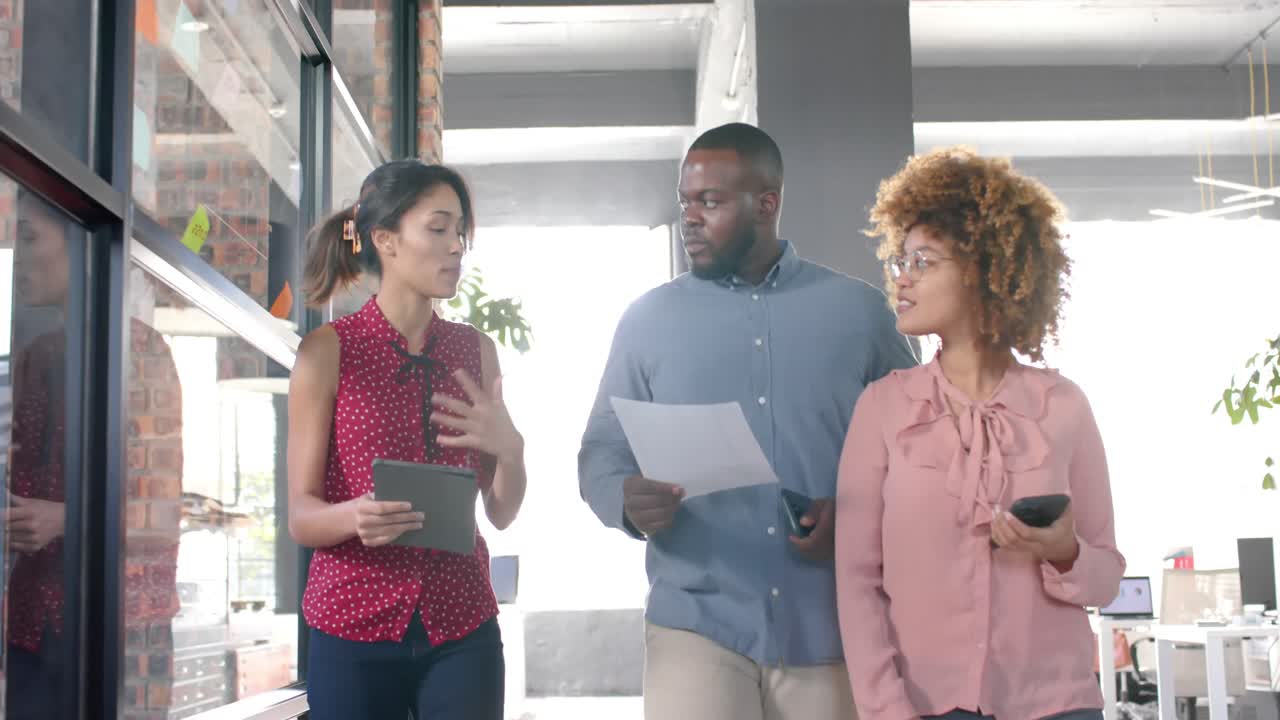 felices colegas diversos con tableta, documento y teléfono caminando en la oficina hablando, cámara lenta