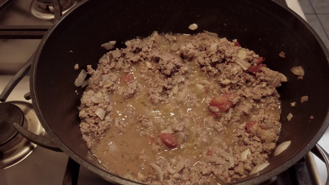 No person, non-stick pan ground beef tomato sauce simmering, side profile shot.