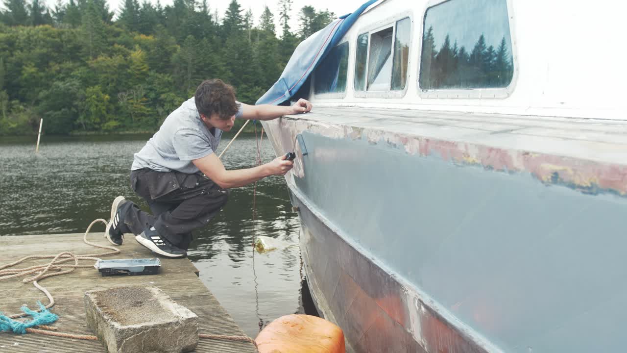 de cerca, hombre caucásico pintando un barco de madera con primer mientras está atracado