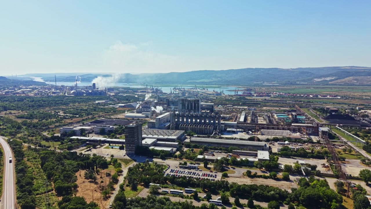 Industria y paisaje a lo largo del río con fábricas, humo y una carretera en primer plano en un día soleado