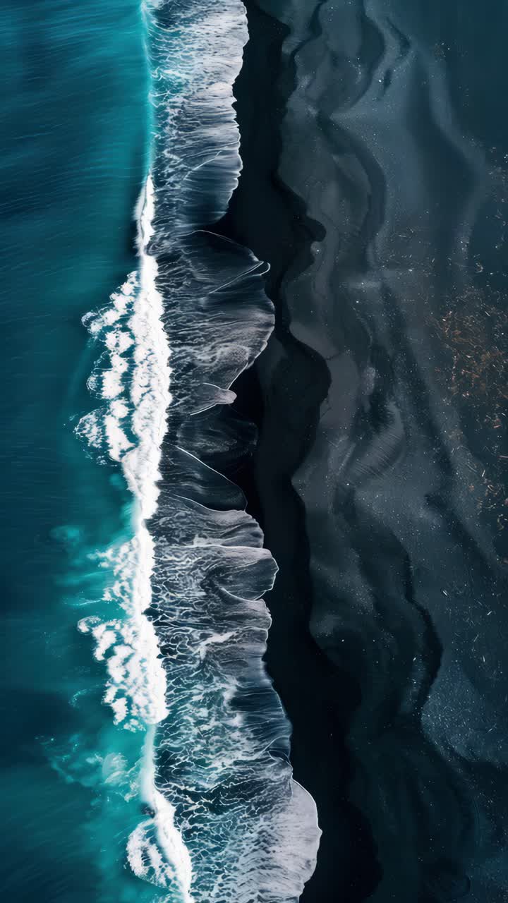 Aerial view of waves crashing on a dark beach, creating a striking contrast