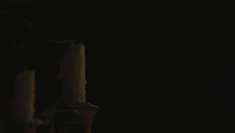 a close up of two white candles lit on a candelabra and being blown out by the wind