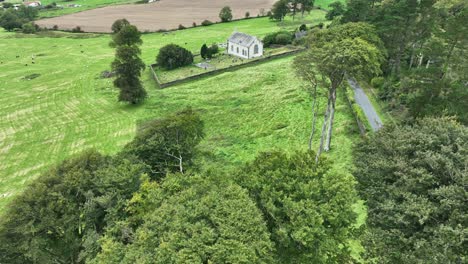 aerial flying low over trees to a small church in the waterford countryside ireland at harvest time