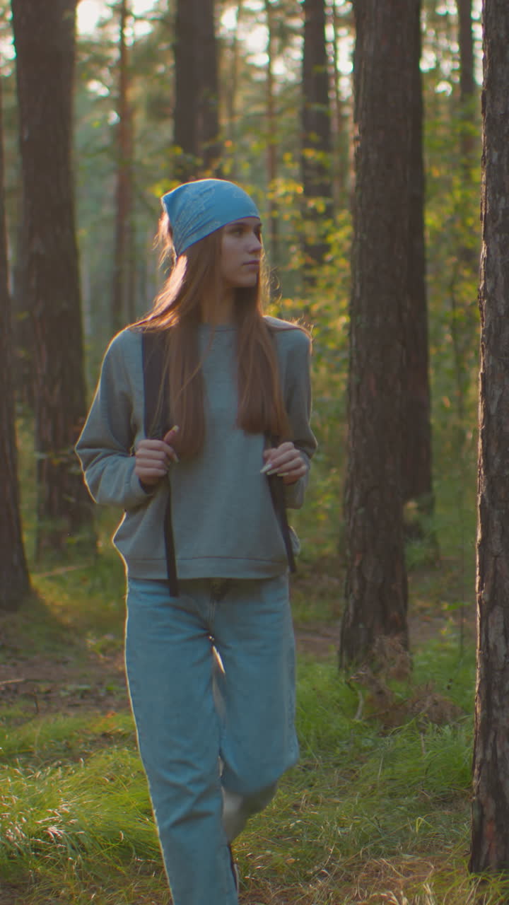Young woman walking through a tranquil forest, holding backpack straps ...