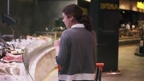 young female costumer trying to choose seafood at a supermarket. walking along the row