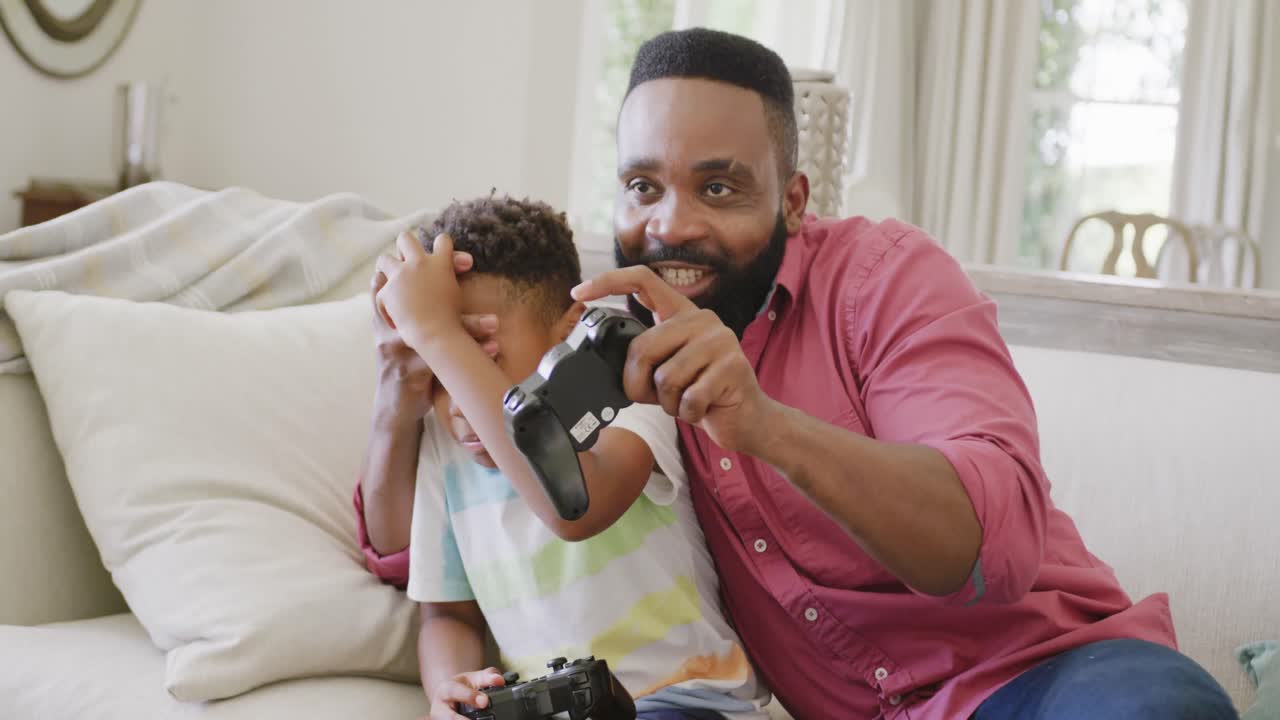 Happy african american father and son watching playing video games together, in slow motion