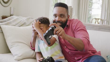 happy african american father and son watching playing video games together, in slow motion