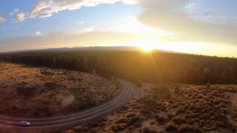 single car travels along a highway road during sunset over the mountains