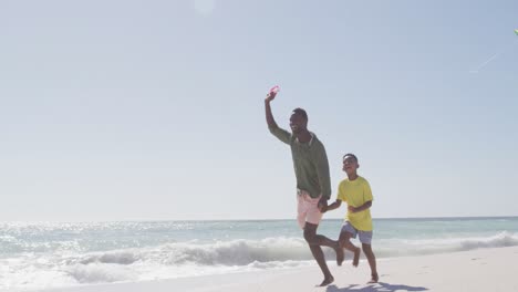 Smiling-african-american-father-with-son-flying-kite-on-sunny-beach