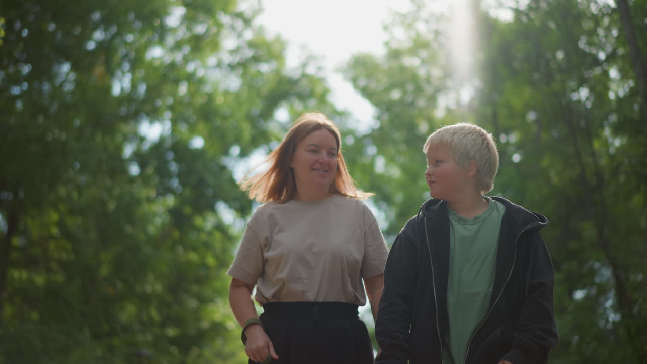 Adults And Children Walking Outdoors, Women And Boys Taking Leisurely Walk, Mother And Son Meander Through Lush Shaded Park, Woman And Young Boy Ambling Under Bright Sunlight In Park