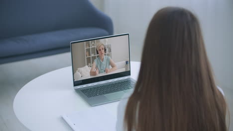 Distance-learning-online-education.-A-woman-studies-at-home-and-Elearning-zoom-video-call.-A-home-distance-learning.-Over-shoulder-view.