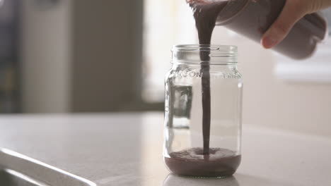 a woman's hand pours a smoothie into a reusable glass mason jar in slow motion