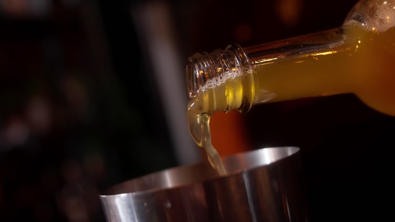 Liquido dorato versato in uno shaker di metallo in un bar poco illuminato, bolle al rallentatore