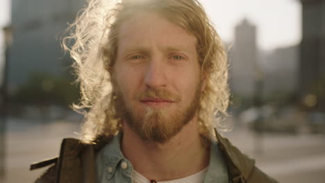 close-up-portrait-of-blonde-bearded-man-pensive-student-looking-calm-at-camera-urban-city-background