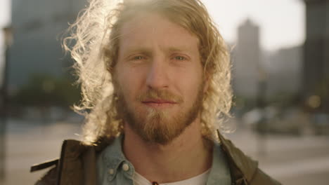 close up portrait of blonde bearded man pensive student looking calm at camera urban city background