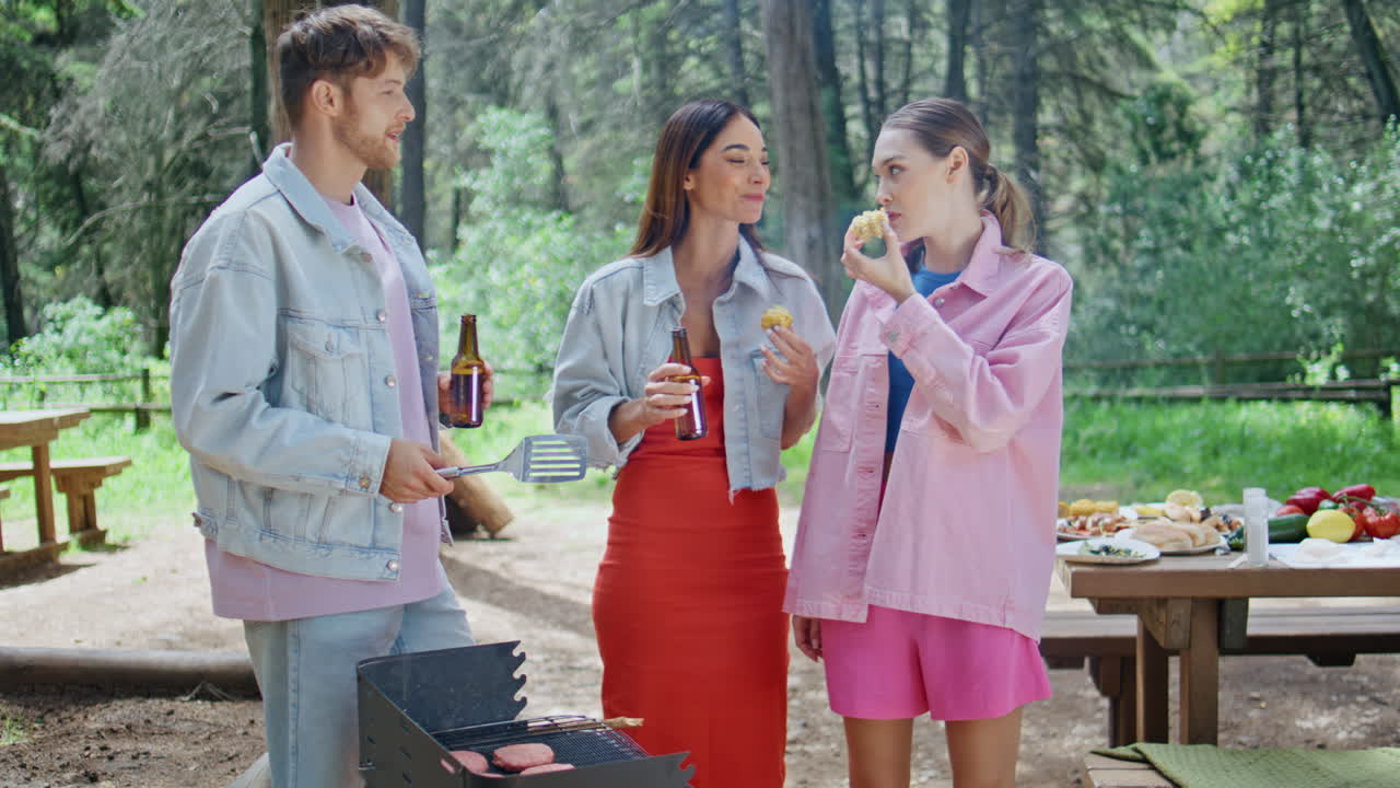 Three friends talking barbeque eating grilling food at picnic. Happy colleagues