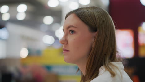 close-up of young woman gazing forward with thoughtful expression in a vibrant indoor setting, featuring colorful blurred background and soft lighting