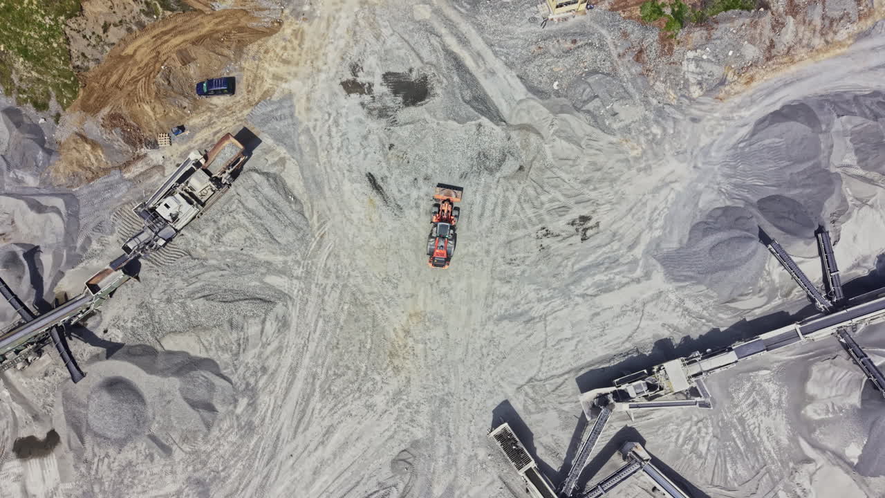 Workers and machinery operating in a granite quarry during daylight hours with various equipment on site for stone extraction and processing