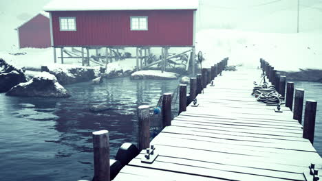 snow-covered wooden dock leading to red cabin in winter wonderland