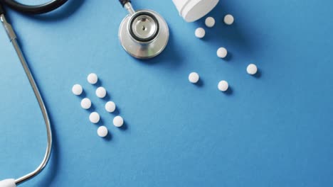 Video-of-stethoscope-with-syringe-and-white-pills-on-blue-background-with-copy-space