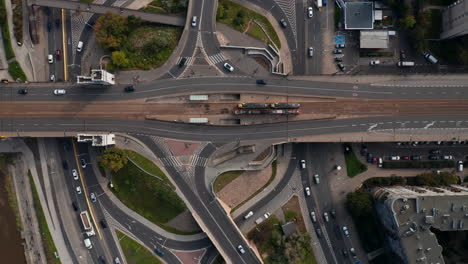 Aerial-birds-eye-overhead-top-down-view-of-traffic-on-road-intersection-on-riverbank.-Trams-stopping-at-tram-stop.-Transport-in-city.-Warsaw,-Poland