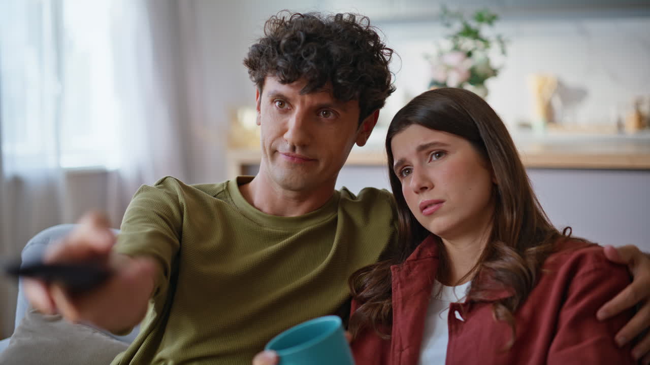 Young boyfriend switching channels remote controller closeup. Couple watching tv