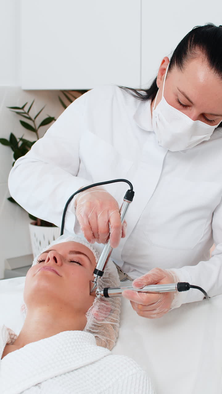 Voksen kvinde modtager foryngende ansigtsbehandling på en kosmetologklinik af en professionel kosmetolog.