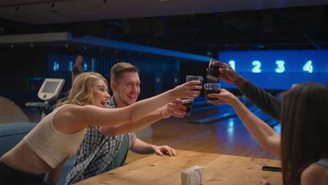 en el club de bolos un grupo de amigos golpea con vasos sentados en la mesa y felizmente hablando y riendo.