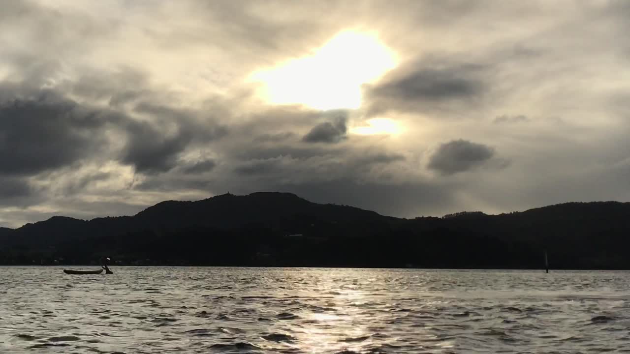 흐린 일몰 동안 물결치는 물 위에 떠 있는 입구 한가운데에 정박한 카약