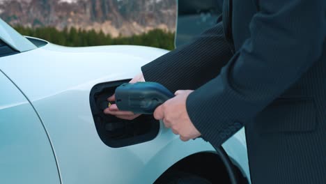 progressive businessman recharge ev car from charging point in rural mountain.