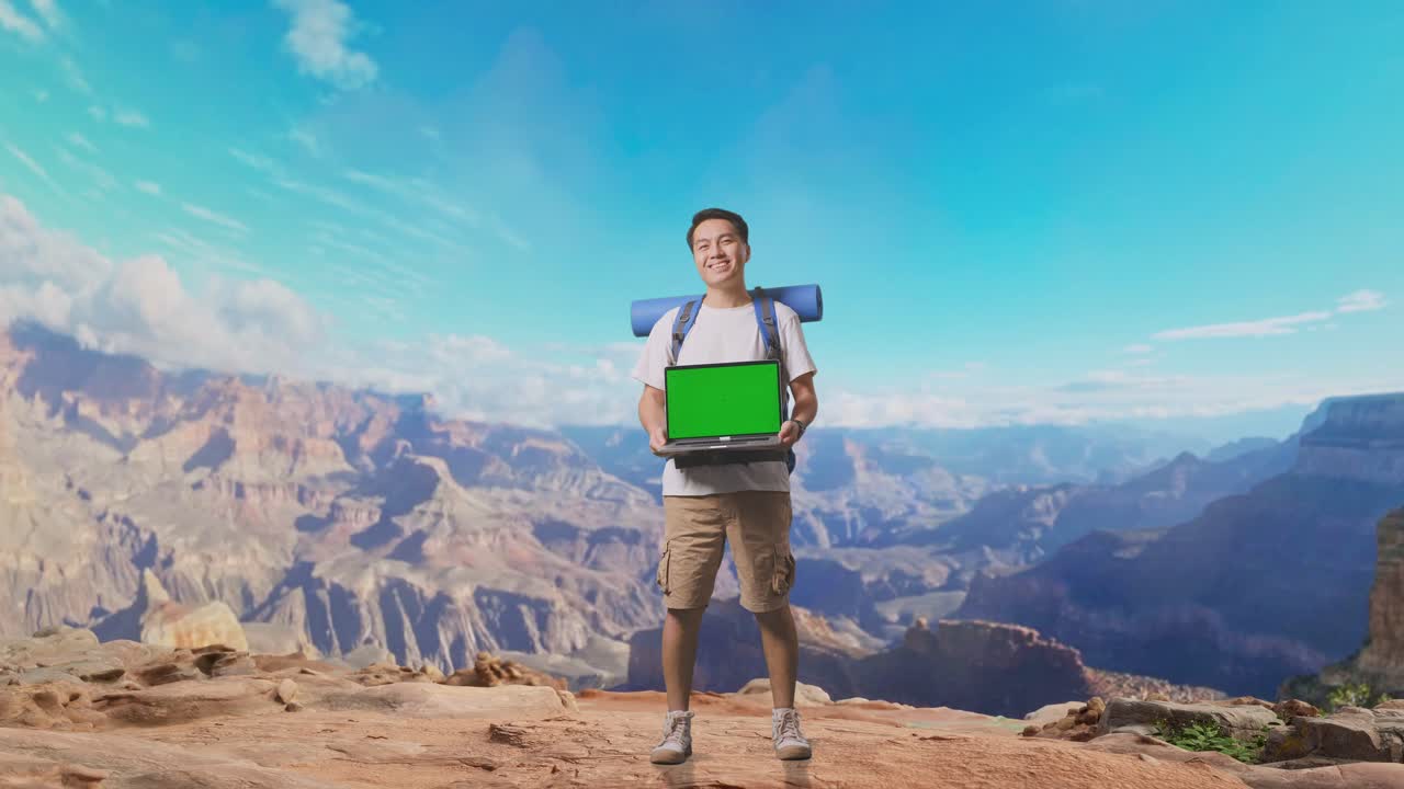 Full Body Of Asian Male Hiker With Mountaineering Backpack Smiling And Showing Mock Up Green Screen Laptop While Traveling At The Top Of Mountain