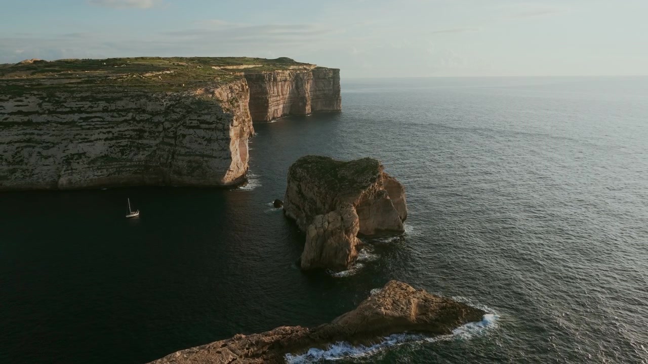 Aerial View of Majestic Sea Cliffs and Rock Formations with a Sailboat