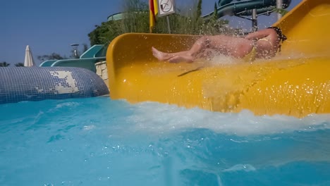 descenso del tobogán acuático en un parque acuático de vacaciones. cámara lenta en un tobogán acuático vacaciones familiares, una mujer en bikini desciende del tobogán en una piscina de agua azul salpicando gotas de agua.