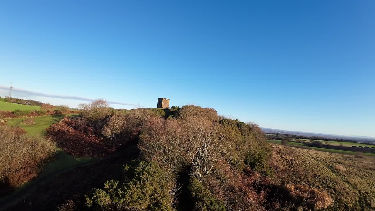 Drone FPV in volo verso il faro di Billinge Hill, tra i campi e i boschi del Lancashire in autunno.
