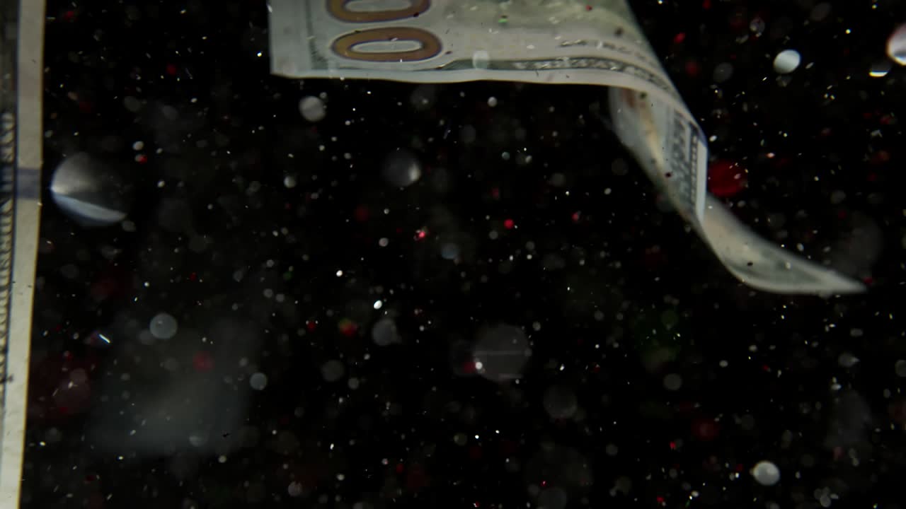 Falling flying american dollar banknotes and flying mixing with the glitter sparkles on a black background in 4K Loopable. High quality falling Dollar banknotes in 4K. Video is Loopable